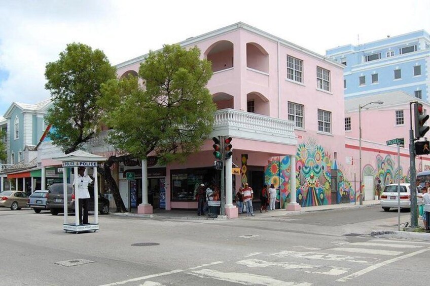A pink building with a colorful mural, a police booth, and a tree in front. 3