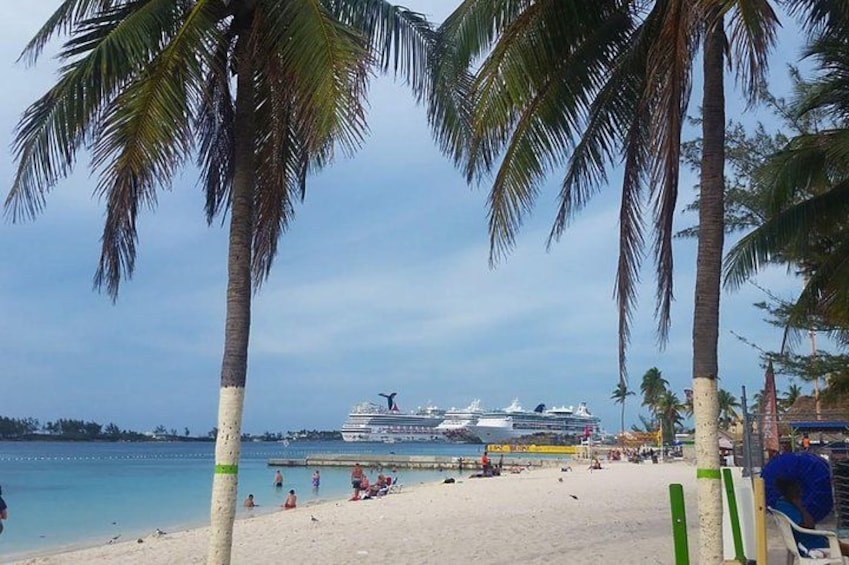 A beach with palm trees, a cruise ship docked, and people on the sand. 2