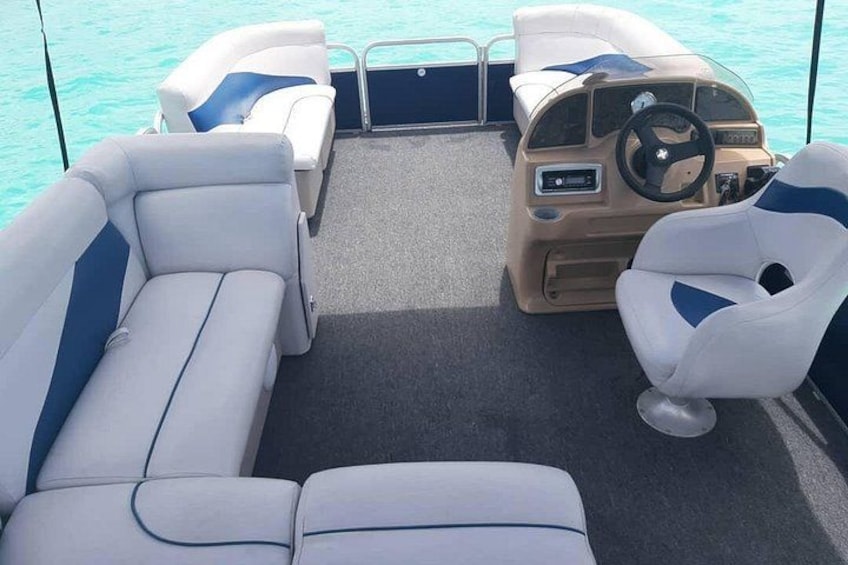 A boat interior with two white cushioned seats, a steering wheel, and a control panel. 2