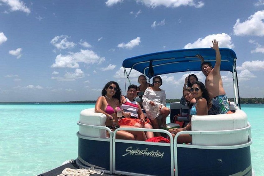 A group of people on a boat with a blue canopy, surrounded by clear turquoise water. 3