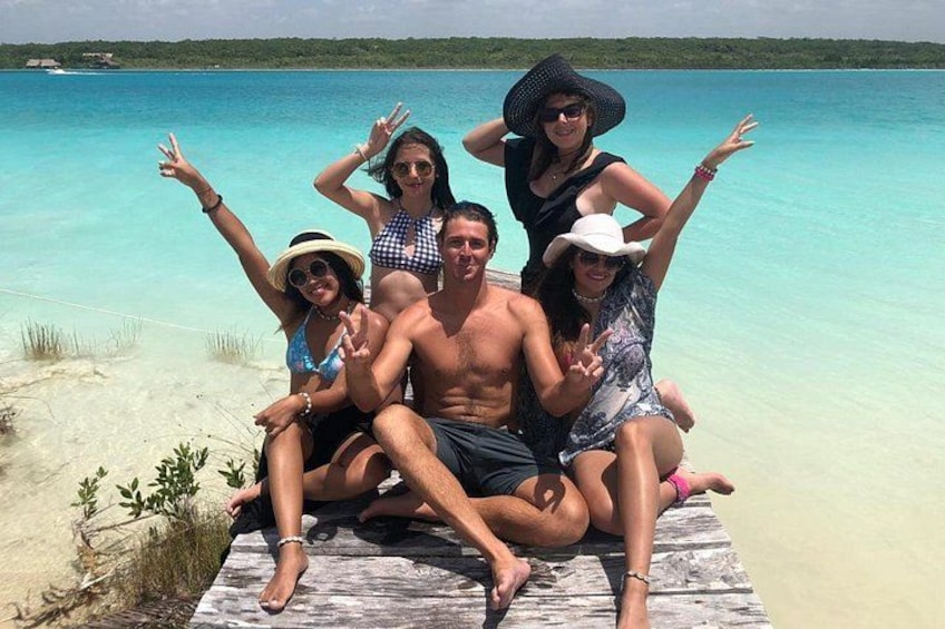 A group of people sitting on a wooden dock by a clear blue sea. 5