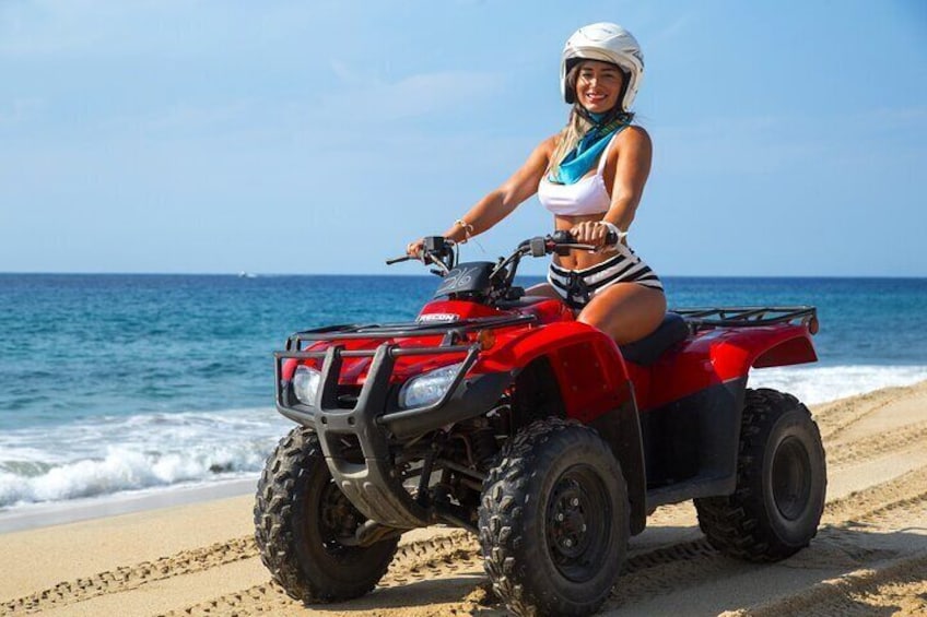 Une personne conduit un quad rouge sur une plage de sable, avec l’océan en arrière-plan. 2
