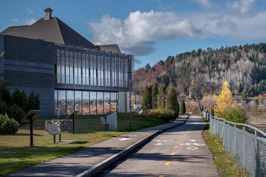 A modern building with large windows, a paved path, and a hilly landscape in the background. 2