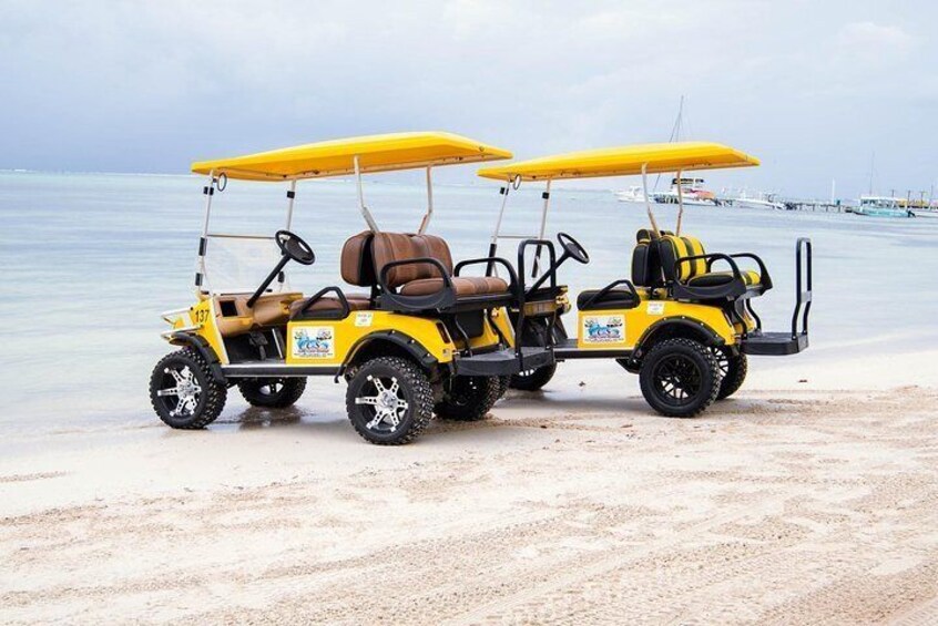 To gule golfbiler med kalecher parkeret på en sandstrand. 4