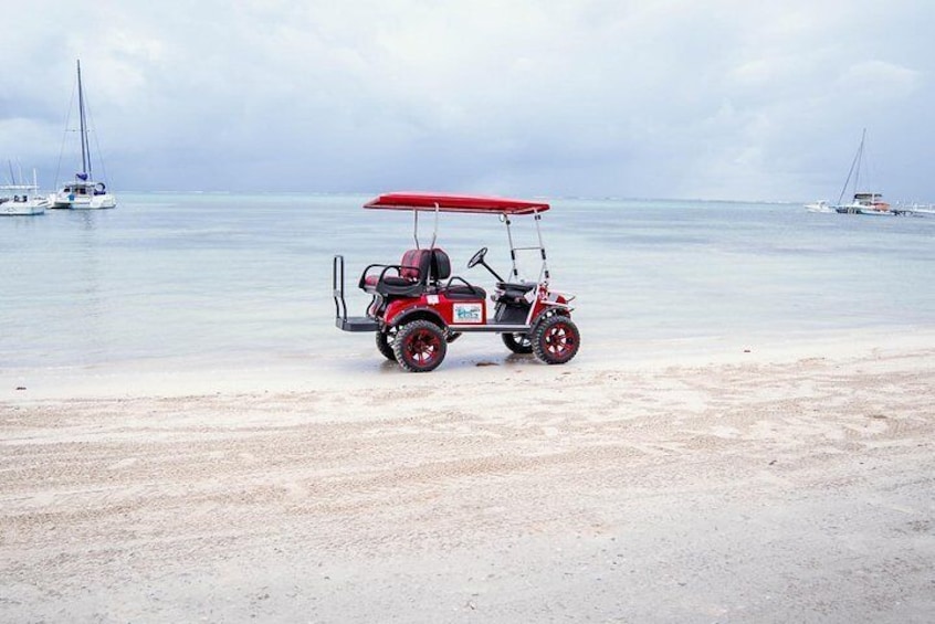 En rød golfbil på en sandstrand med både i baggrunden. 1