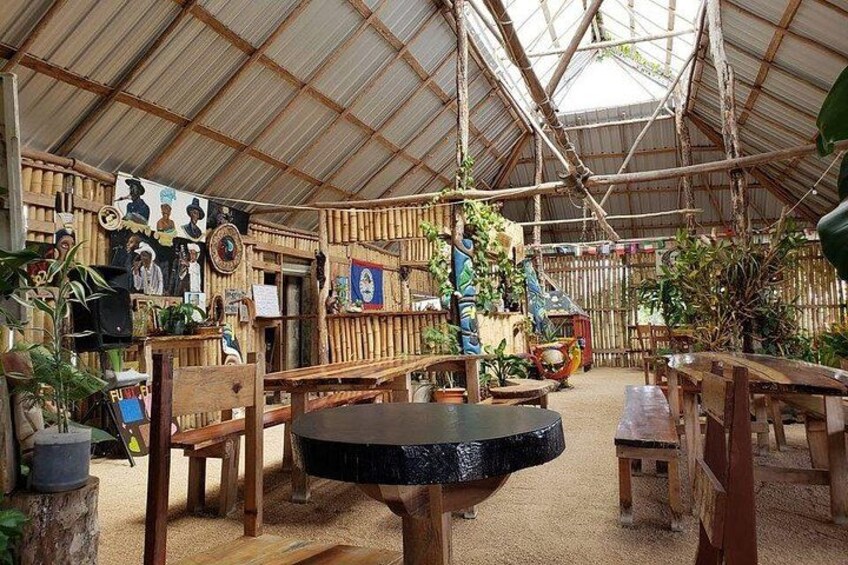 A rustic wooden interior with bamboo walls, a thatched roof, and various plants. 2