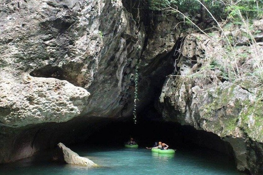 A cave entrance with a rope hanging down, a person in a green kayak, and a large rock formation. 1