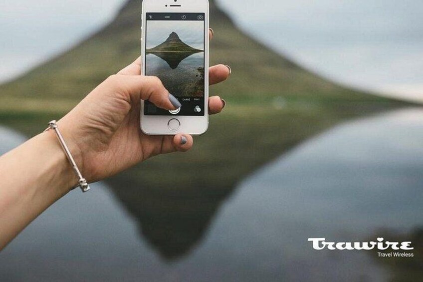 Una mano sosteniendo un teléfono inteligente que muestra un paisaje con una montaña y el reflejo del agua. 2
