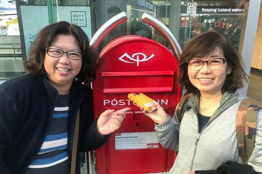 Dos personas de pie junto a un buzón rojo, sosteniendo una postal en la mano. 5