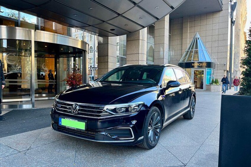 En svart Volkswagen-SUV parkerad framför en byggnad med en entré av glas och ett blått markis. 2