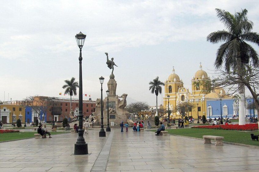 A plaza with a statue, a church, and palm trees. 1