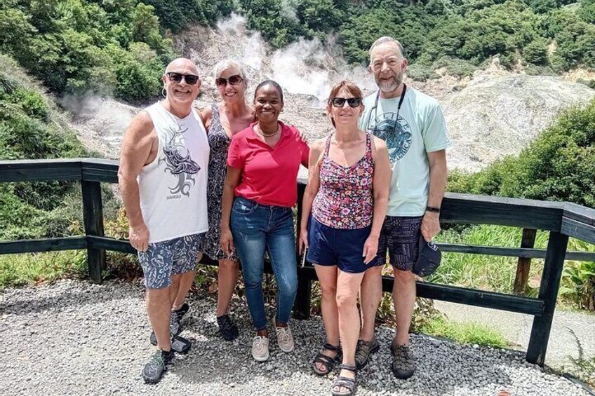 A group of people standing on a gravel path with a wooden railing, surrounded by greenery and a rocky landscape. 4