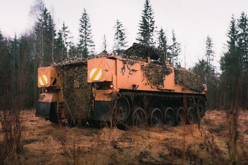 A military vehicle with camouflage netting in a forested area. 3