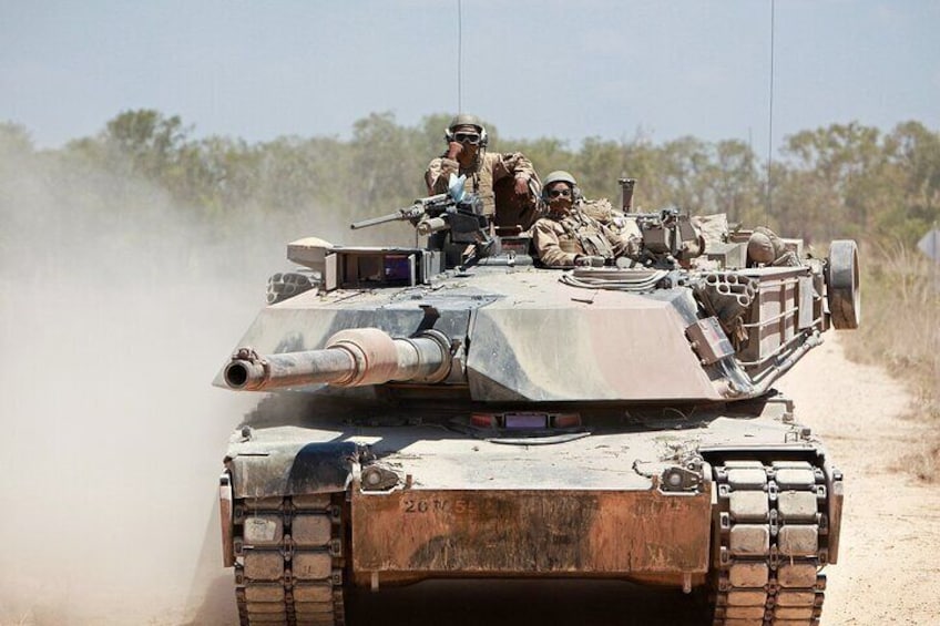 A military tank with soldiers on top, moving through a dusty, open landscape. 2