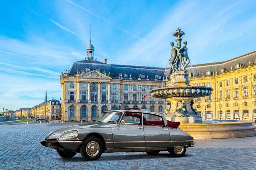 A vintage car parked in front of a historic building with a fountain. 2