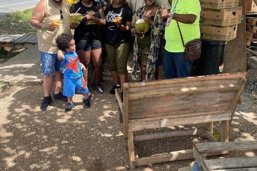 Un grupo de personas de pie al aire libre, con un banco de madera al frente. 3
