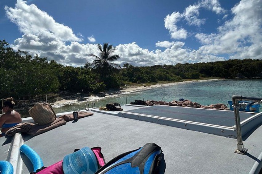 A boat deck with lounge chairs, a person in a swimsuit, and a beach with clear water and palm trees. 3