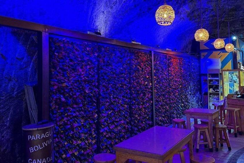 Interior de restaurante con pared iluminada en azul, mesas de madera y luces esféricas colgantes. 2