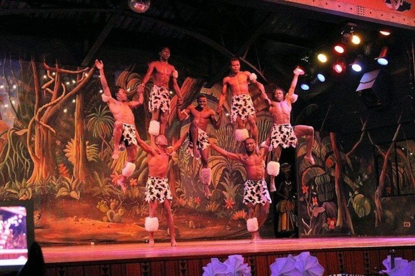 Een podium met optreders in opvallende shorts, een jungledecor en podiumverlichting. 3