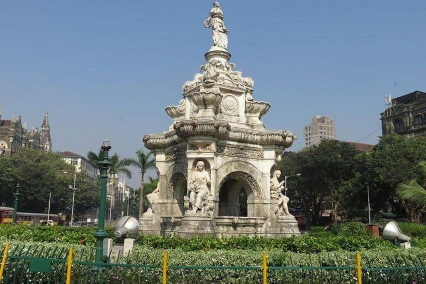 A historical monument with statues and intricate carvings, surrounded by greenery and urban buildings. 3