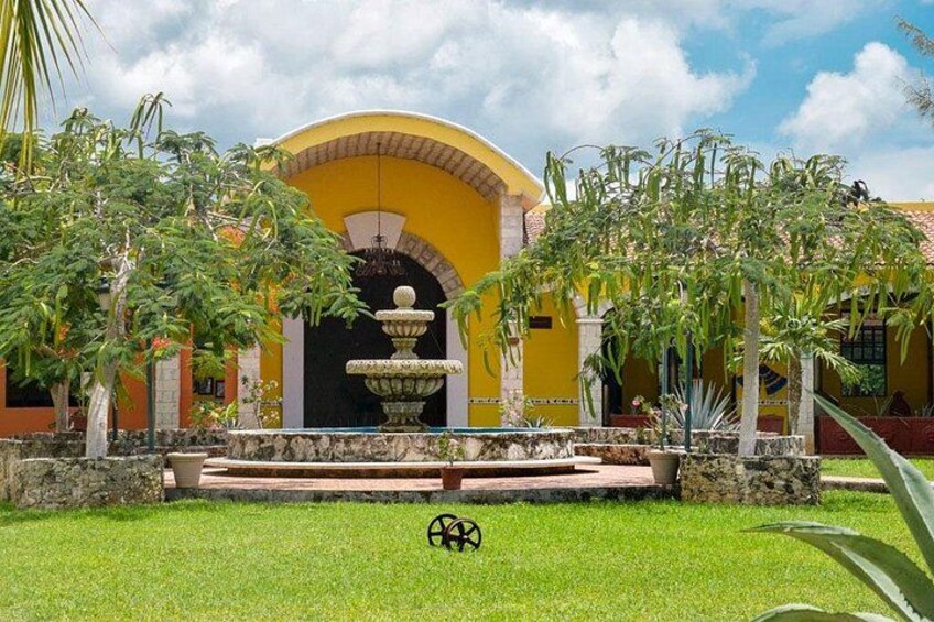A courtyard with a fountain, yellow building, and green grass. 2
