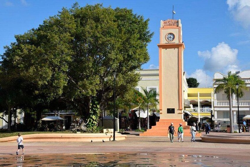 A public square with a clock tower, trees, and people walking. 5