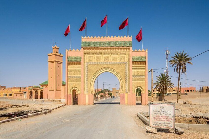 A large archway with multiple flags, a road leading through it, and a signboard in the foreground. 4