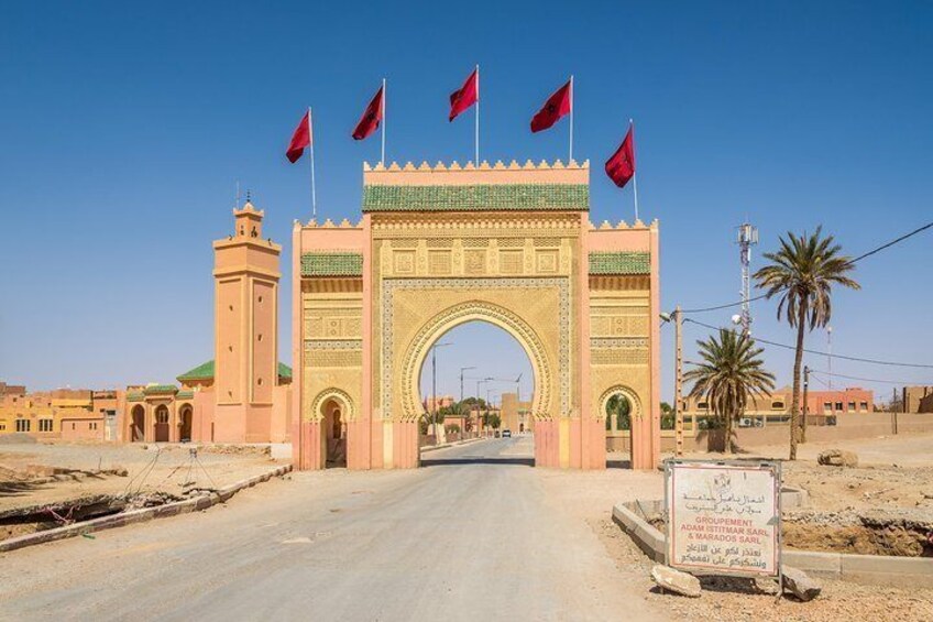A large archway with multiple flags, a road leading through it, and a signboard in the foreground. 4