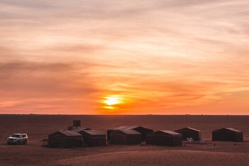 A sunset over a desert landscape with several wooden structures and a car. 2