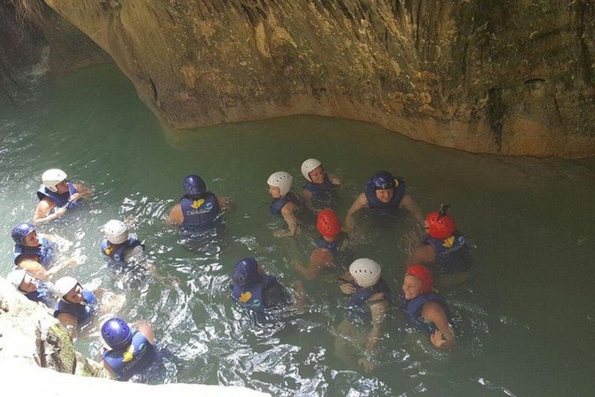 A group of people in water, wearing helmets and life jackets, in a cave-like environment. 2