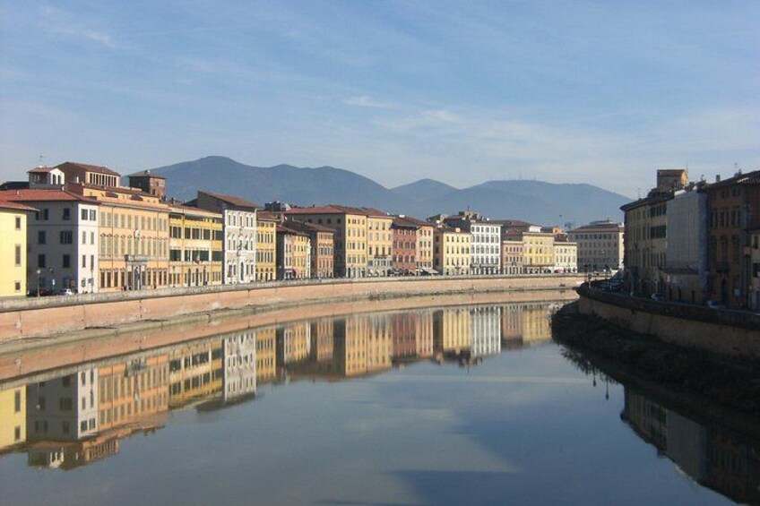 Une rivière paisible où se reflètent les bâtiments, avec des montagnes en arrière-plan et un ciel dégagé. 1