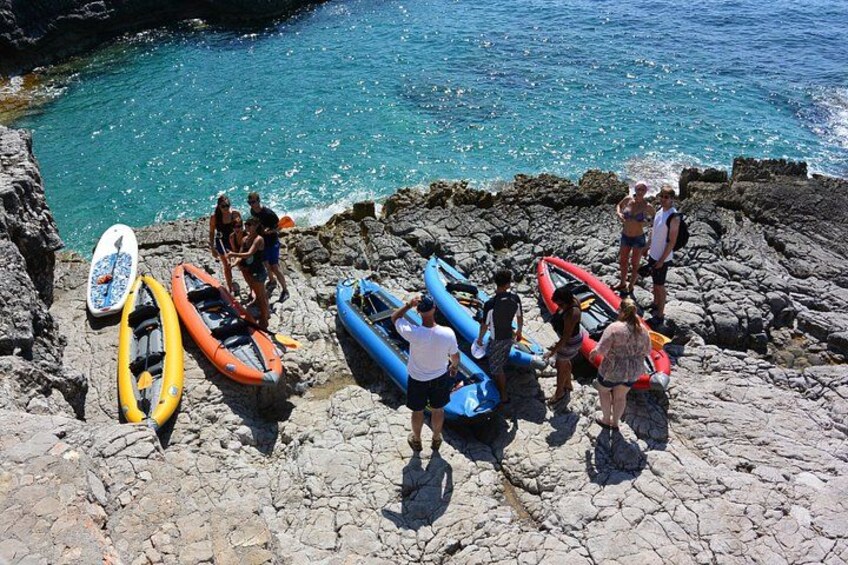 People standing on rocky terrain near a body of water, with several inflatable boats and a surfboard. 2
