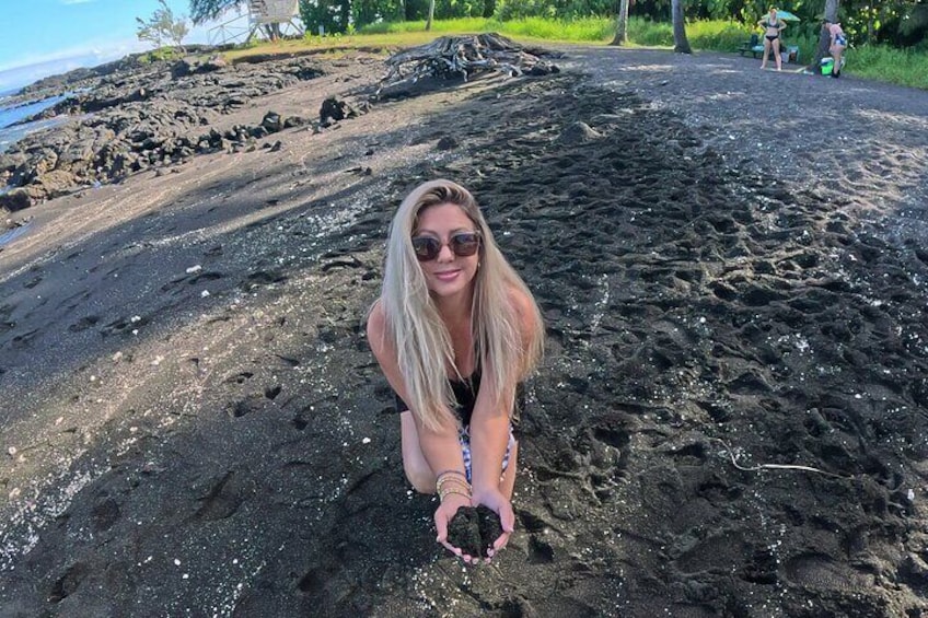 Una persona accovacciata su una spiaggia di roccia vulcanica, con un piccolo oggetto in mano. 4