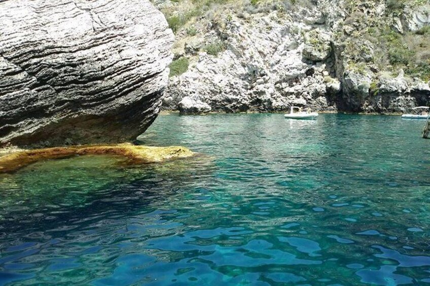 A clear blue sea with a large rock formation and a small boat in the distance. 4