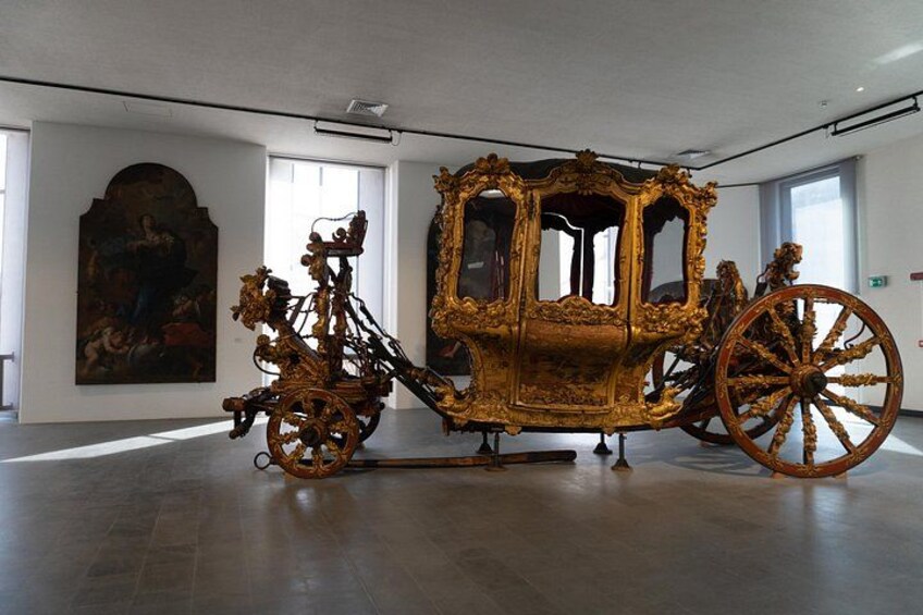 An ornate carriage in a museum with large wheels and intricate design. 3