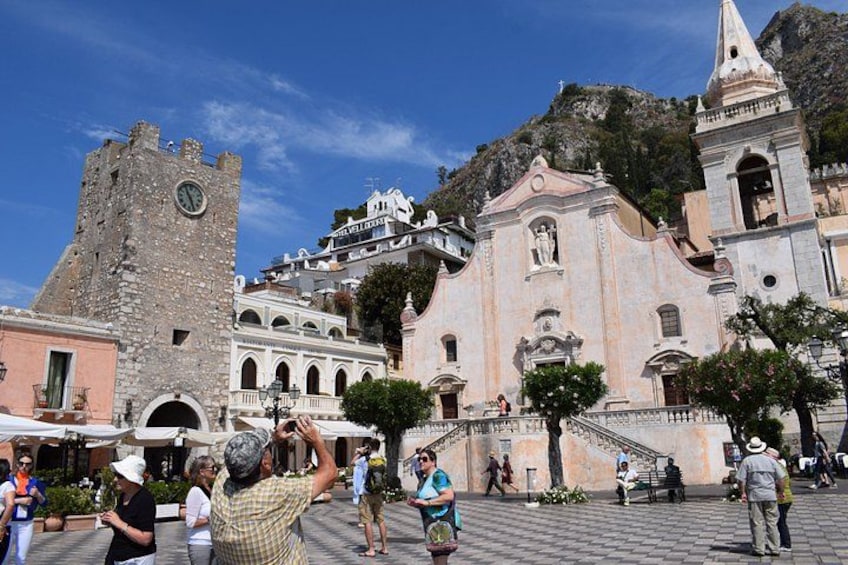 Una plaza histórica con una iglesia destacada, una torre del reloj y montañas al fondo. 2