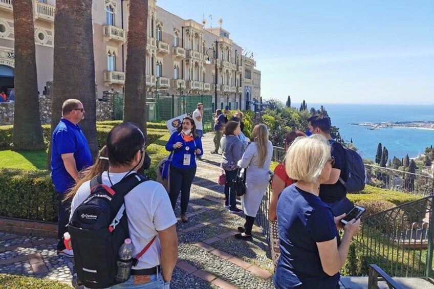 Un grupo de personas caminando por un sendero de piedra, con vistas al mar y edificios al fondo. 5