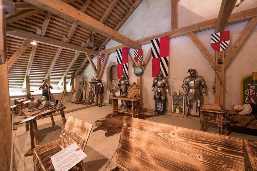 A medieval exhibit with armor, shields, and flags in a wooden-roofed room. 2