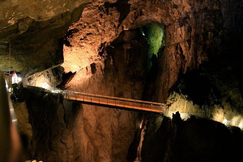 Un puente en una cueva con una formación rocosa iluminada en verde a un lado. 3