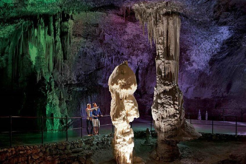 A cave with stalactites and stalagmites, a rope barrier, and two people observing. 3