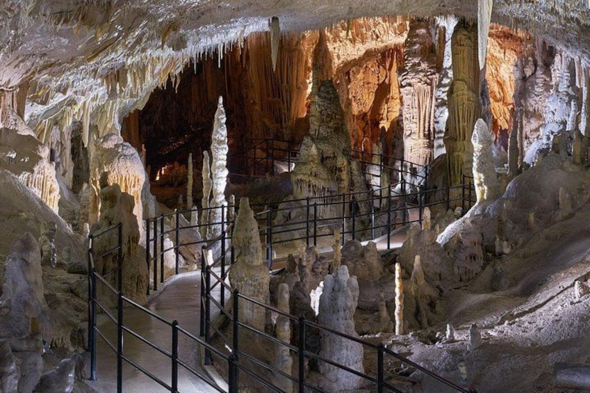 A cave with stalactites and stalagmites, a walkway, and a railing. 3