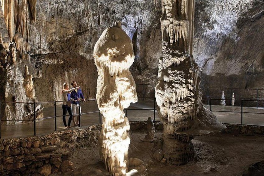 A cave with stalactites and stalagmites, a person standing near the entrance, and a railing for safety. 2
