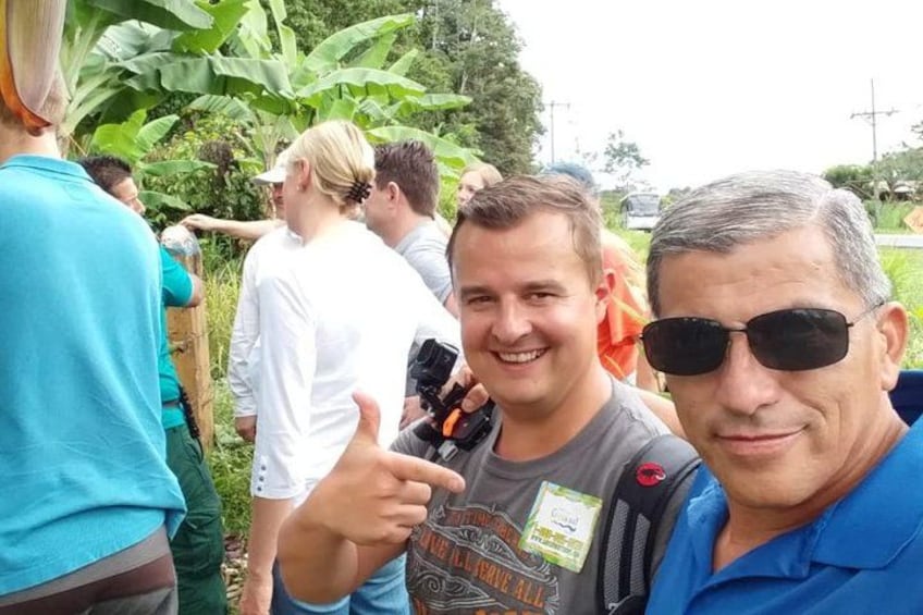 A group of people outdoors, some wearing casual clothing, with greenery and a clear sky in the background. 4