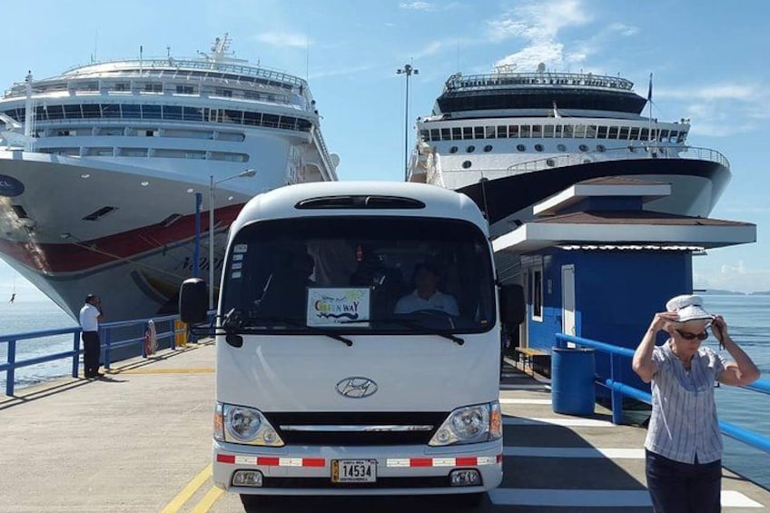 A ferry docked at a pier with a large cruise ship in the background. 2