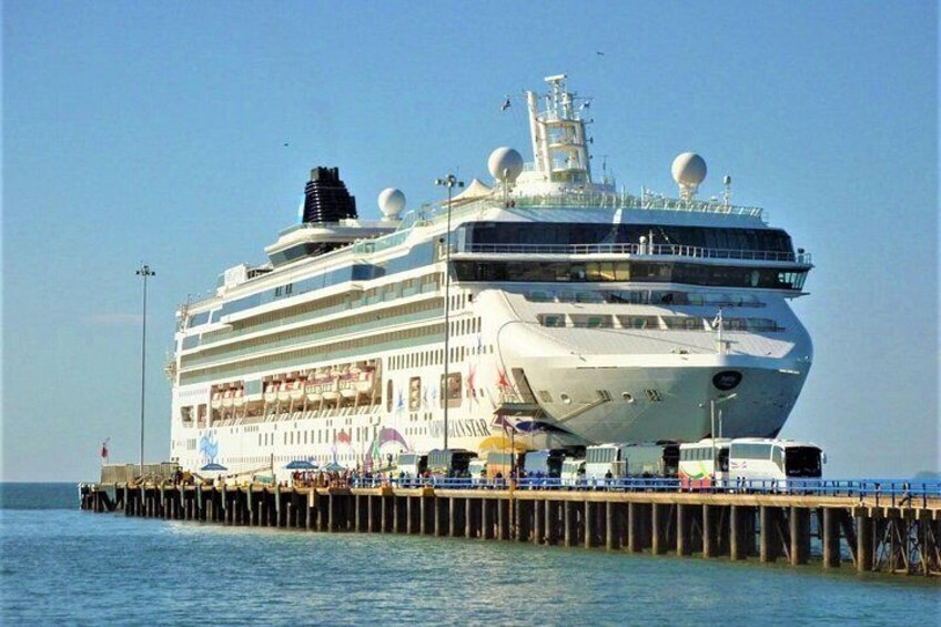 A large cruise ship docked at a pier with people walking along the pier. 3