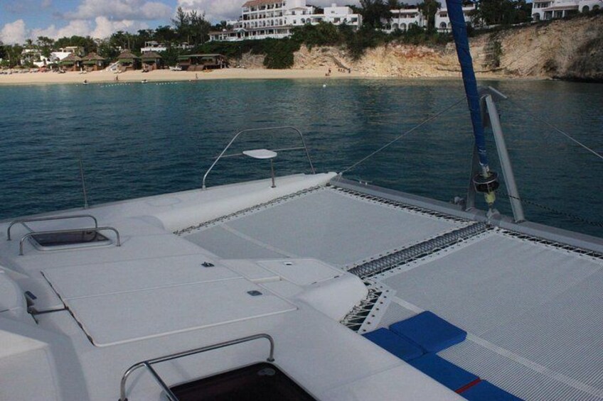 Cubierta de barco con asientos y barandilla, mar tranquilo y playa con edificios al fondo. 5