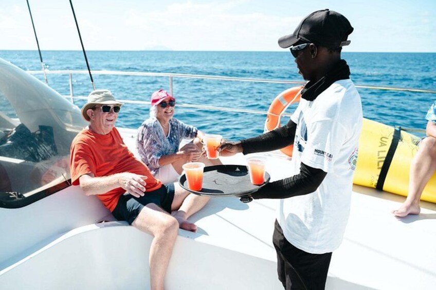 Una persona sirviendo bebidas en un barco, con vista despejada al océano y un flotador de salvamento al fondo. 3