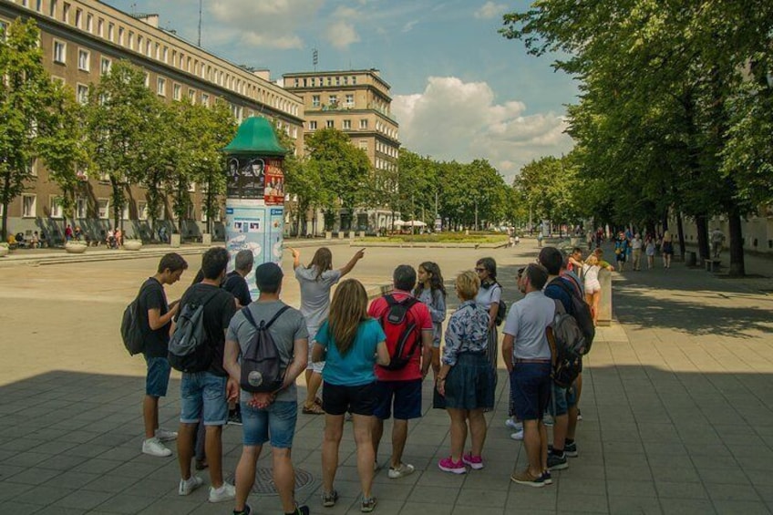 A group of people standing in a public square, facing a building with a green roof. 2