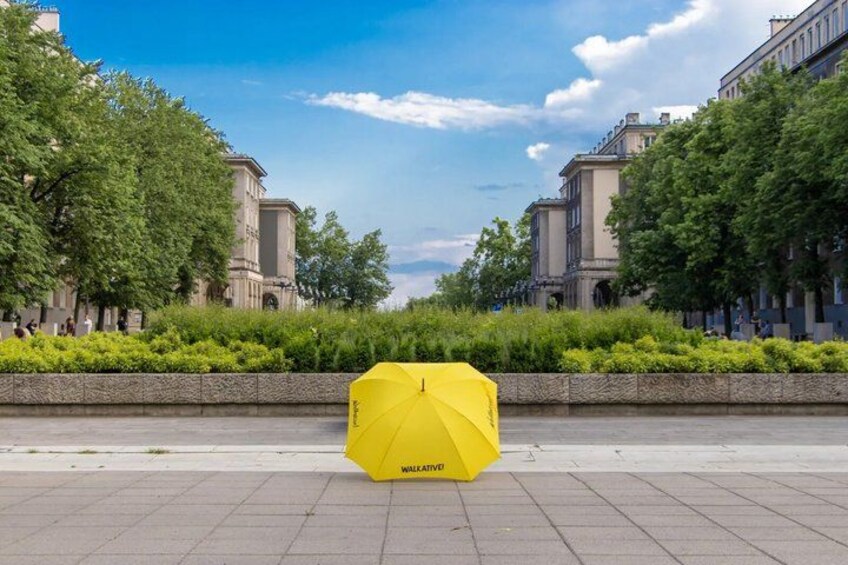 A yellow umbrella on a paved walkway with buildings and trees in the background. 5