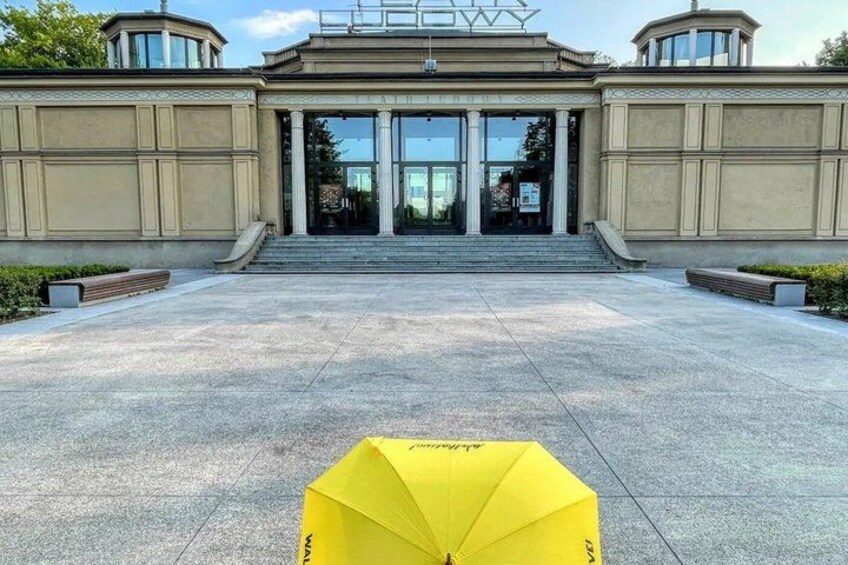 A building entrance with steps leading up to it, a yellow umbrella in the foreground, and a clear sky. 2